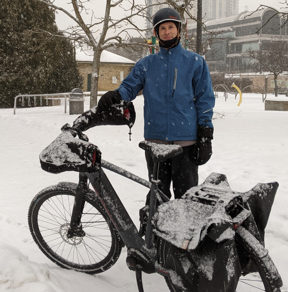 Andrew, covered in snow standing in front of his bike.